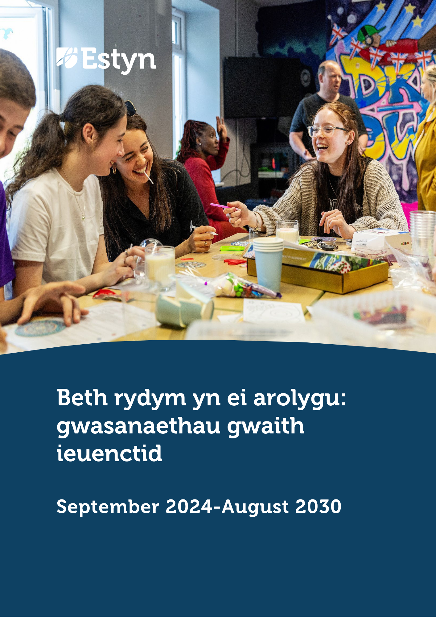 Grŵp o bobl ifanc ac oedolion yn eistedd o amgylch bwrdd yn cymryd rhan mewn gweithgaredd celf a chrefft creadigol mewn lleoliad cymunedol.