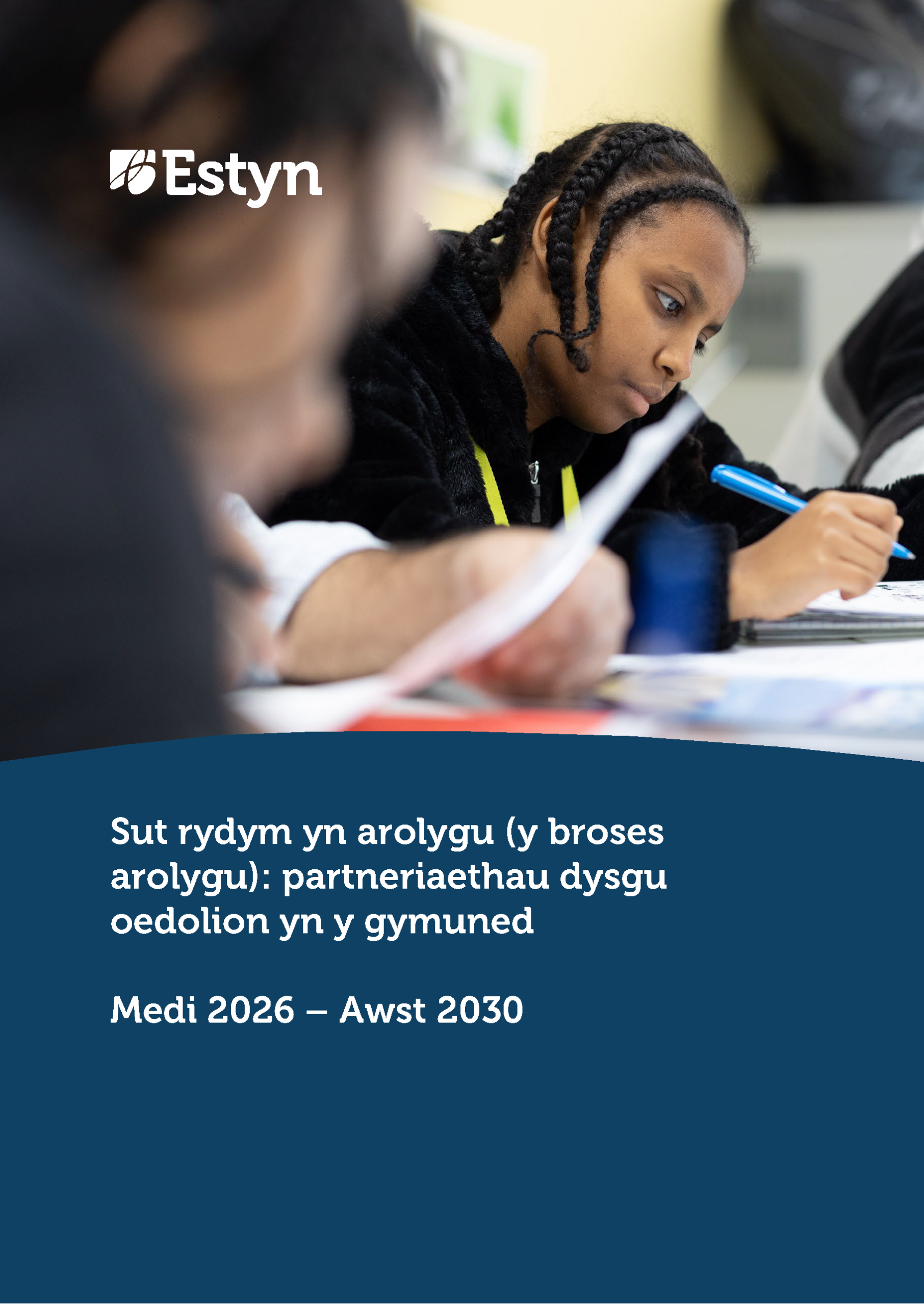 Dysgwr yn canolbwyntio ar dasg ysgrifenedig yn yr ystafell ddosbarth, yn gwneud nodiadau yn ystod gwers tra bod dysgwyr eraill yn gweithio gerllaw.