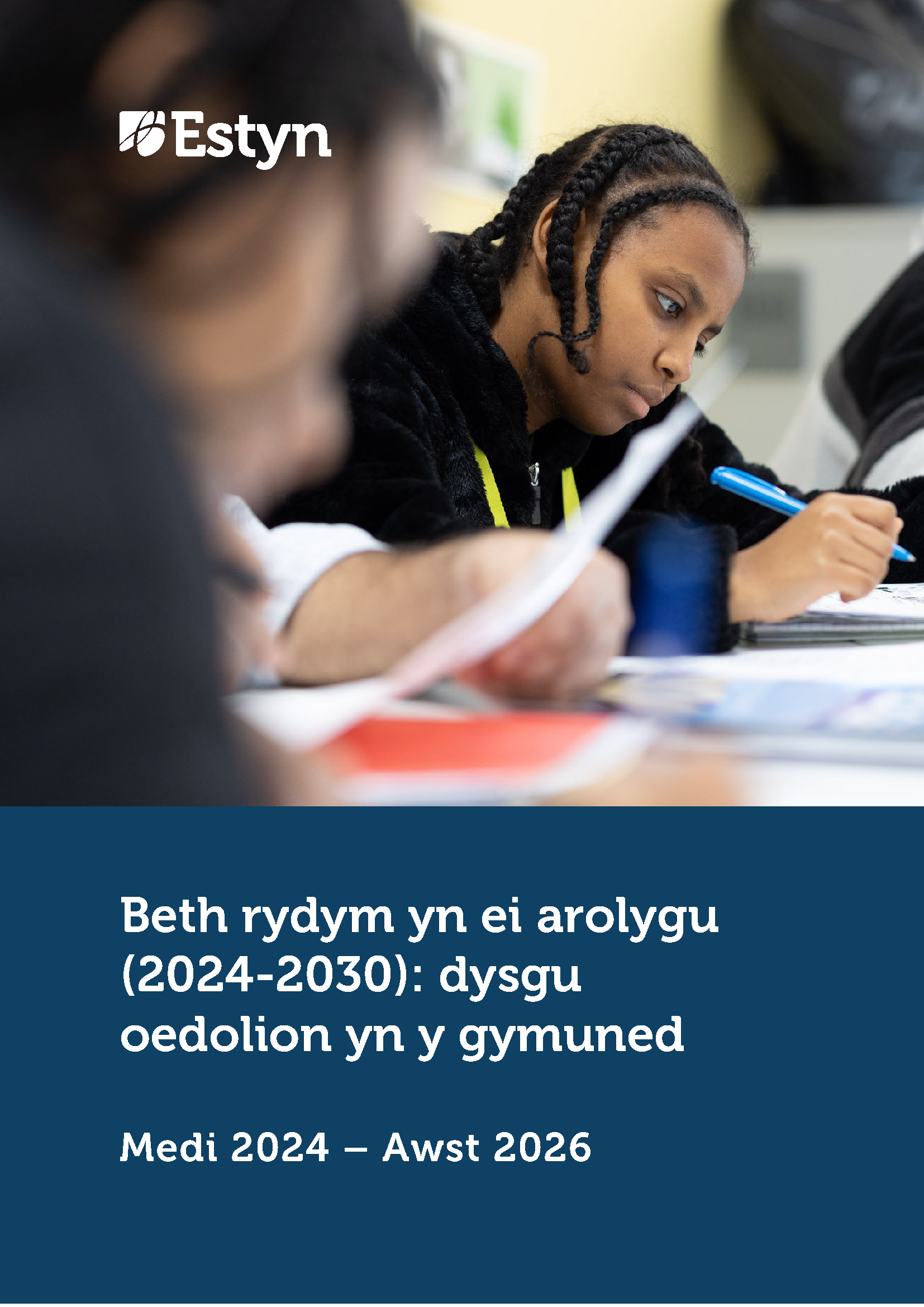 Dysgwr yn canolbwyntio ar dasg ysgrifenedig yn yr ystafell ddosbarth, yn gwneud nodiadau yn ystod gwers tra bod dysgwyr eraill yn gweithio gerllaw.