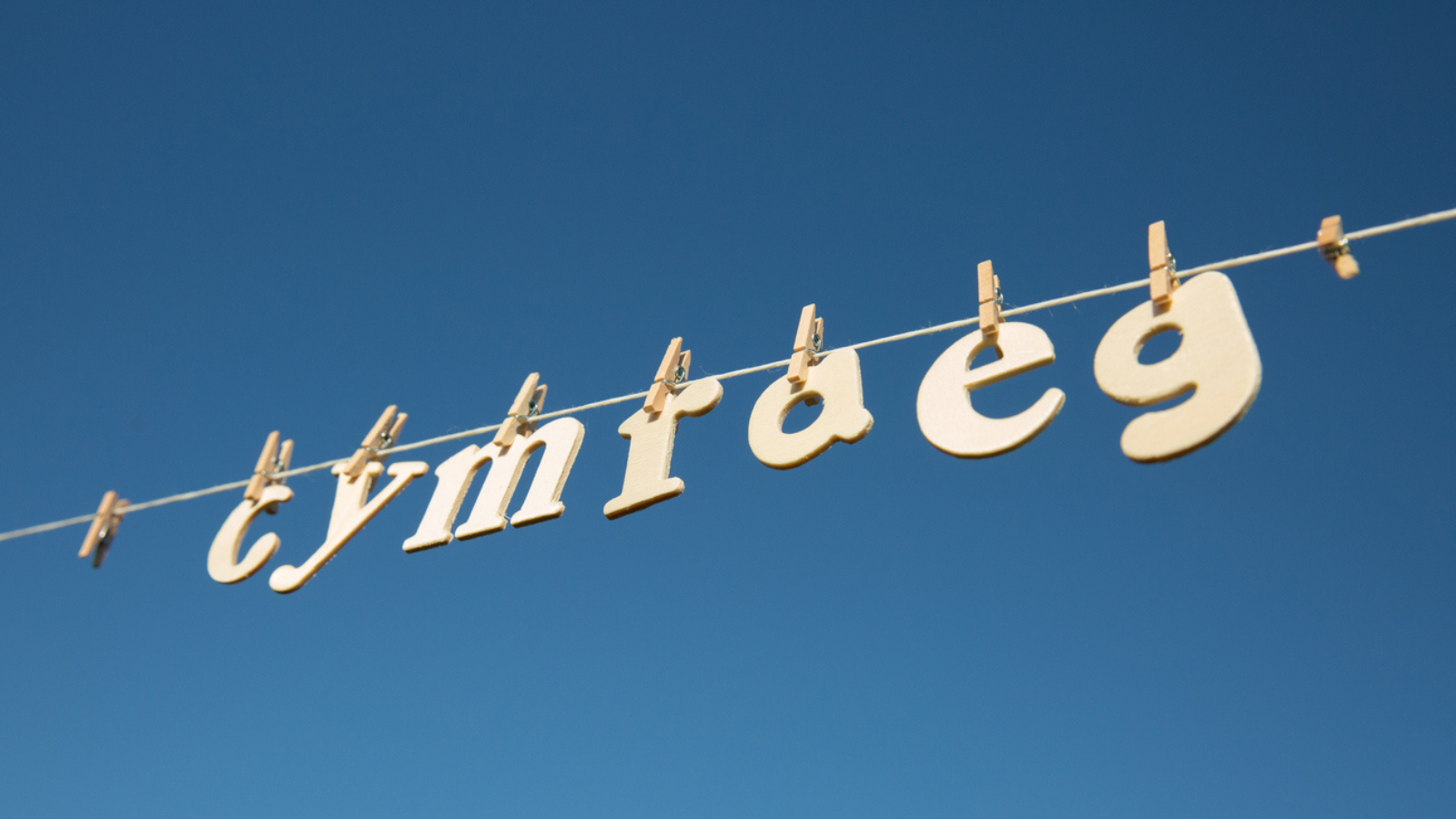 Letters spelling 'cymraeg' which means 'Welsh' in the Welsh language, hanging on a line against a clear blue sky.