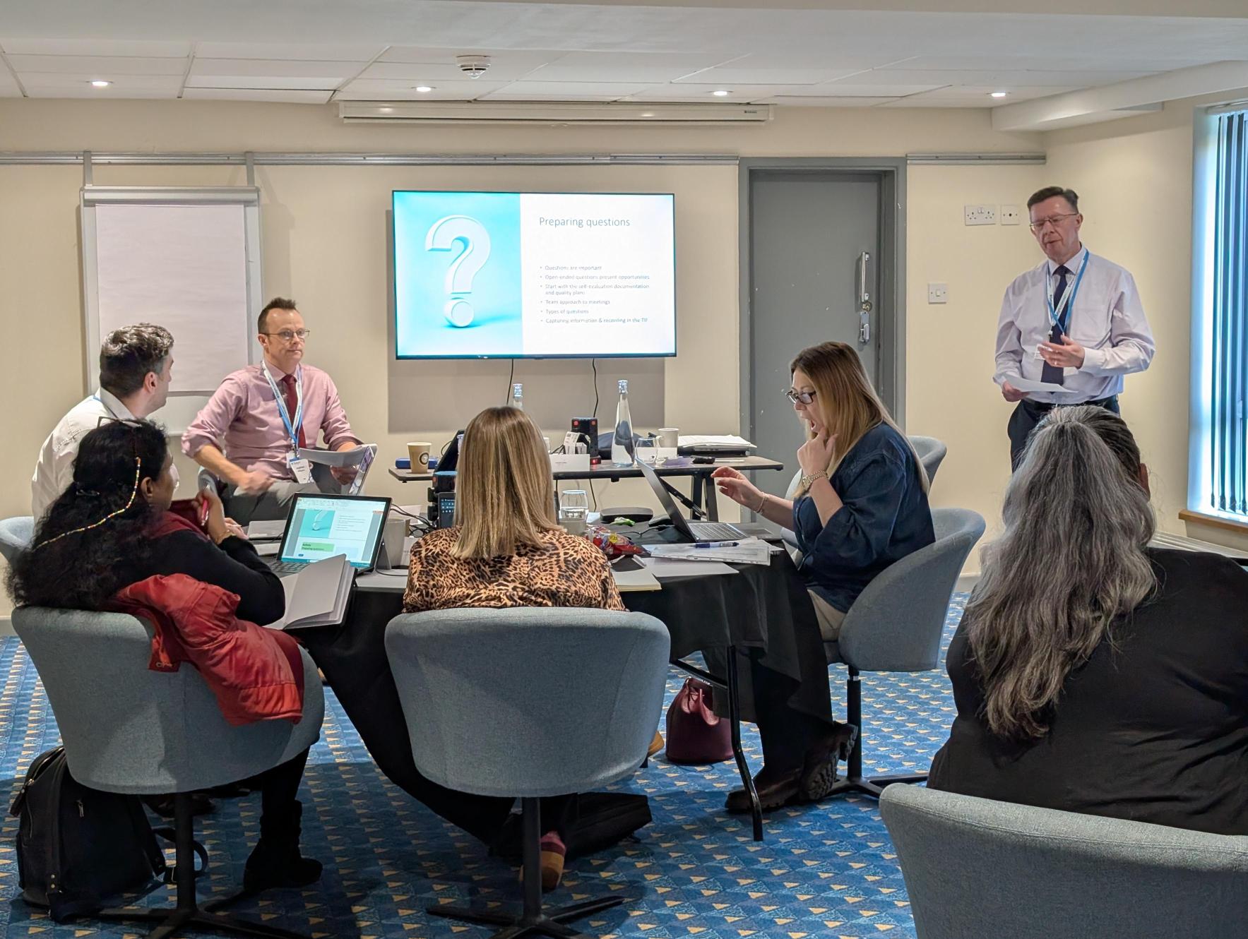 Group of professionals attentively participating in a workshop, with one person standing and presenting.