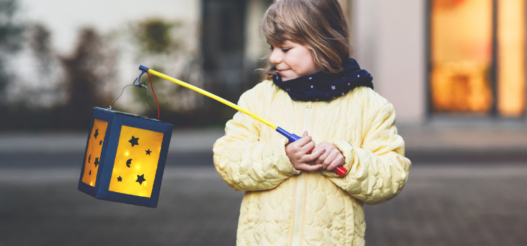 Plentyn yn dal llusern â phatrwm seren ar bolyn, yn gwisgo siaced felen a sgarff las, yn sefyll y tu allan.