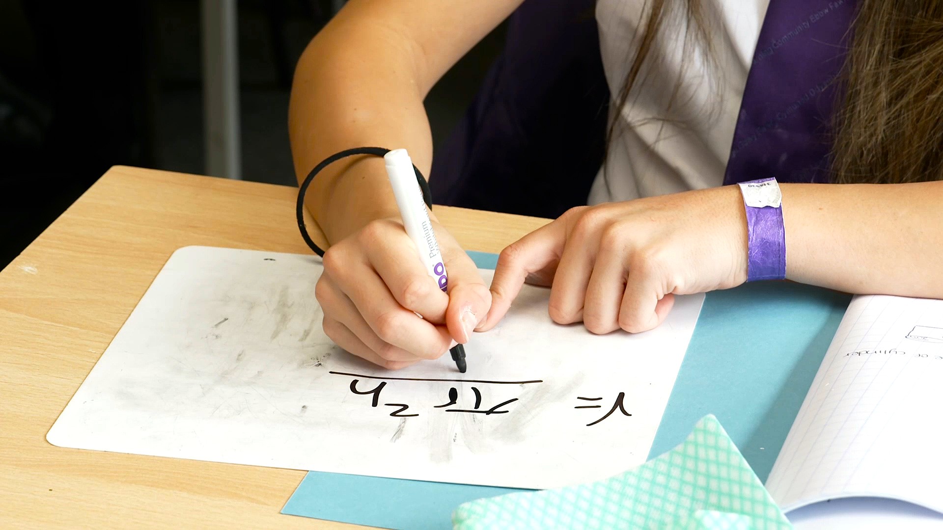 Close up image of a pupil's hand writing a maths equation on a small whiteboard.