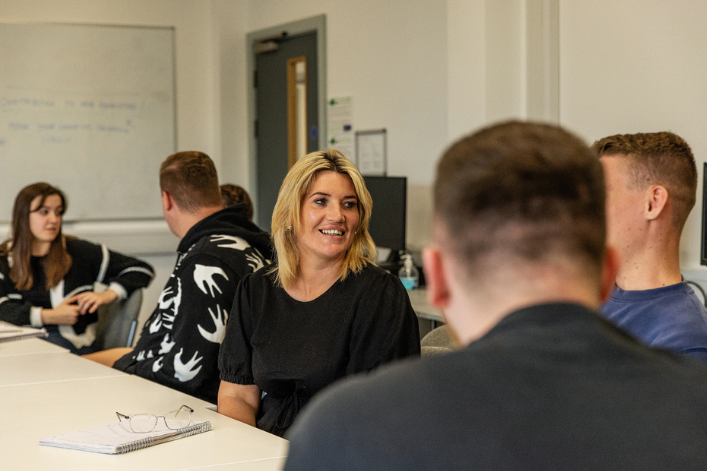 Grŵp o athrawon yn eistedd o amgylch byrddau dosbarth yn cael trafodaeth.