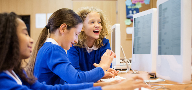 Disgyblion yn defnyddio cyfrifiaduron bwrdd gwaith gyda’i gilydd yn ystod gwers TGCh yn y dosbarth.